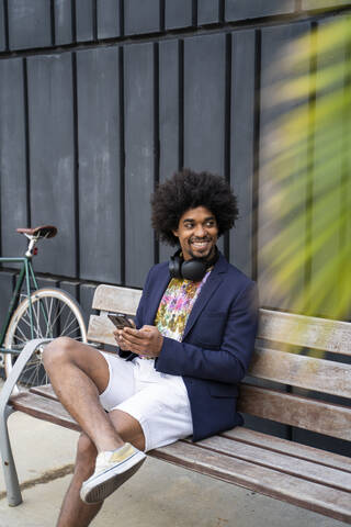 Smiling stylish man with cell phone sitting on a bench stock photo