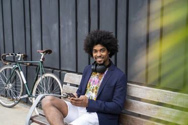 Portrait of stylish man with cell phone sitting on a bench - AFVF03851