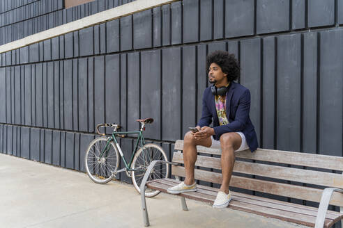 Stylish man with cell phone sitting on a bench - AFVF03856