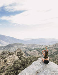 Rear view of sportive young woman sitting on rocky viewpoint - LJF00713