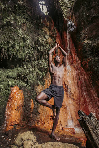 Mann übt Yoga am Wasserfall, Baumstellung, lizenzfreies Stockfoto