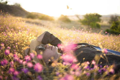 Junge Frau mit Sonnenhut auf einer Wiese liegend bei Sonnenuntergang - KNTF03081
