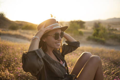 Junge Frau sitzt bei Sonnenuntergang auf einer Wiese - KNTF03084