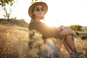 Junge Frau mit Sonnenhut und auf einer Wiese sitzend bei Sonnenuntergang - KNTF03086