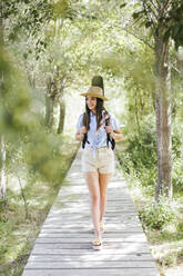 Young woman with guitar case walking on wooden walkway - LJF00746
