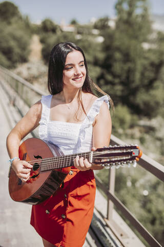 Junge Frau spielt Gitarre, steht auf einer Brücke, lizenzfreies Stockfoto