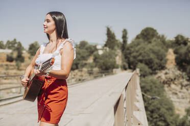 Young woman playing guitar, standing on bridge - LJF00759