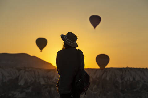 Rückansicht der Silhouette einer jungen Frau, die Heißluftballons betrachtet, während sie an Land in Goreme, Kappadokien, Türkei steht, lizenzfreies Stockfoto