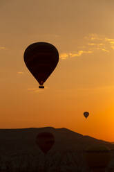 Silhouette Heißluftballons fliegen über Landschaft in Kappadokien gegen Himmel bei Sonnenuntergang, Türkei - KNTF03098