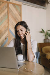 Junge Geschäftsfrau mit Laptop telefoniert am Tisch in einem Café - ALBF00974