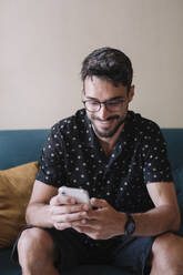 Smiling man sitting on a couch using cell phone - ALBF00975