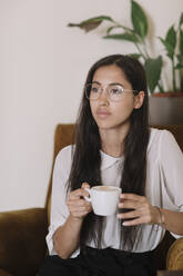 Junge Frau mit einer Tasse Kaffee in einem Sessel in einem Café sitzend - ALBF00976