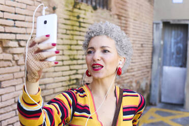 Portrait of mature woman with red lips and grey hair taking selfie with cell phone - RTBF01316