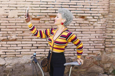 Lächelnde reife Frau mit Fahrrad nimmt Selfie mit Handy - RTBF01317