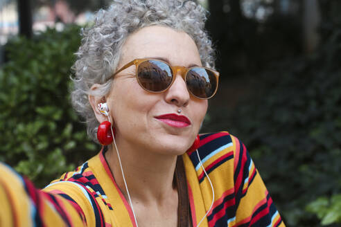 Portrait of pierced mature woman wearing sunglasses and earphones - RTBF01333