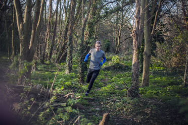 Young man jogging through woods - AJOF00010
