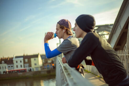 Zwei junge Männer trinken Wasser nach einem Lauf an der Themse, London, UK - AJOF00012