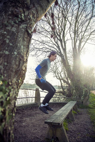 Junger sportlicher Mann springt auf eine Holzbank, lizenzfreies Stockfoto