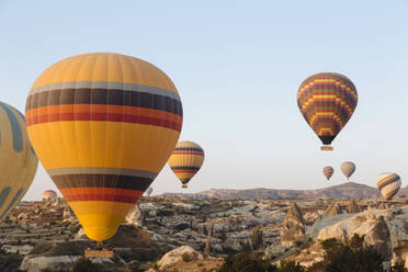 Bunte Heißluftballons fliegen über felsige Landschaft gegen klaren Himmel in Kappadokien, Türkei - KNTF03248