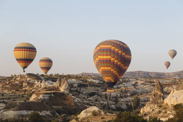 Bunte Heißluftballons fliegen über Landschaft gegen klaren Himmel in Kappadokien, Türkei - KNTF03249