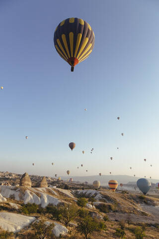 Bunte Heißluftballons fliegen über felsige Landschaft in Kappadokien gegen klaren Himmel, Kappadokien, Türkei, lizenzfreies Stockfoto