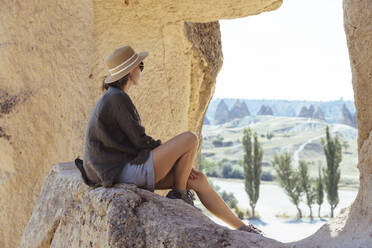 Side view of young woman sitting on rock at Goreme village, Cappadocia, Turkey - KNTF03252