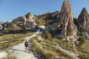 Rear view of young woman walking on road against clear blue sky in Goreme, Cappadocia, Turkey - KNTF03268