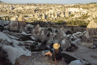 Junge Frau betrachtet die Landschaft, während sie auf einem Felsen in Goreme, Kappadokien, Türkei, sitzt - KNTF03269