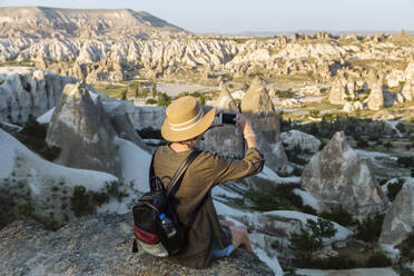 Rear view of young woman photographing landscape with smart phone at Goreme, Cappadocia, Turkey - KNTF03270