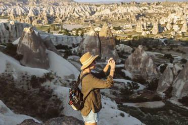 Seitenansicht einer jungen Frau, die mit ihrem Smartphone Felsformationen in Goreme, Kappadokien, Türkei, fotografiert - KNTF03271