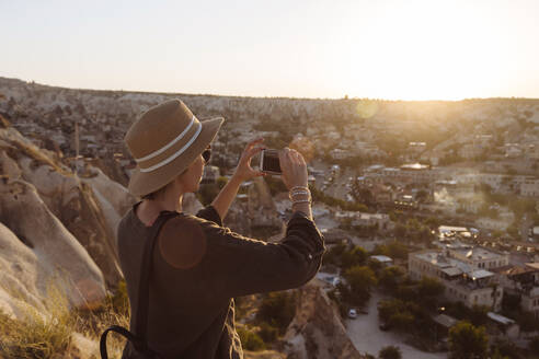 Seitenansicht einer jungen Frau, die während des Sonnenuntergangs mit ihrem Smartphone die Stadt fotografiert, Kappadokien, Türkei - KNTF03273