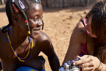 Weiße Frau zeigt einer Frau vom Stamm der Mudimba ein Bild auf ihrer Kamera, Canhimei, Angola - VEGF00569