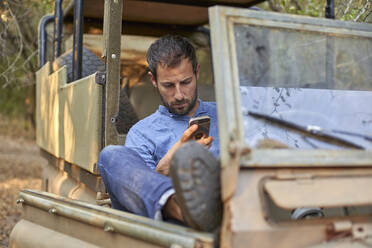 Mann sitzt in einem Geländewagen und benutzt sein Smartphone - VEGF00579