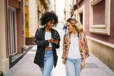 Multikulturelle glückliche Frauen, die in der Stadt spazieren gehen und auf ihr Smartphone schauen - MPPF00005