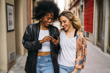 Multicultural happy women walking in the city, looking on smartphone - MPPF00007