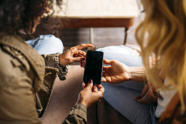 Multikulturelle Frauen schauen in einem Café auf ein Smartphone - MPPF00011