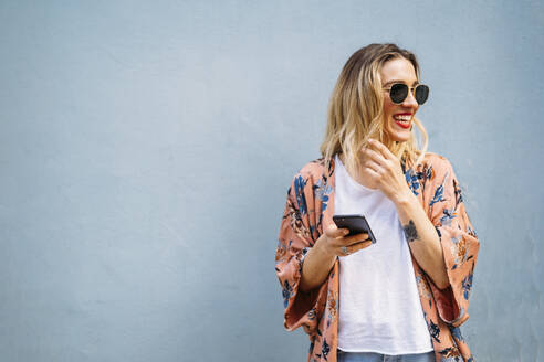 Lächelnde blonde Frau mit Smartphone, blauer Hintergrund - MPPF00015