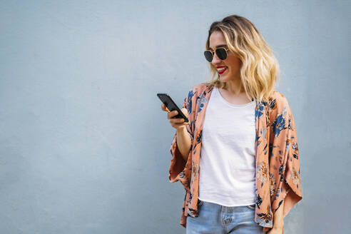 Lächelnde blonde Frau mit Smartphone, blauer Hintergrund - MPPF00016