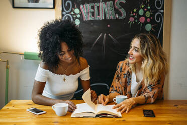 Multikulturelle Frauen unterhalten sich in einem Café und lesen ein Buch - MPPF00031