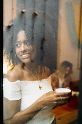 Frau mit einer Tasse Kaffee, die aus dem Fenster schaut, in einem Cafe - MPPF00034