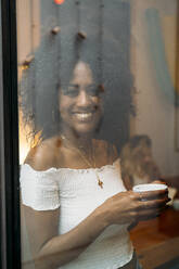 Frau mit einer Tasse Kaffee, die aus dem Fenster schaut, in einem Cafe - MPPF00035