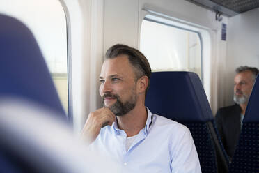 Älterer Mann sitzt in einem Zug und schaut aus dem Fenster - FKF03553