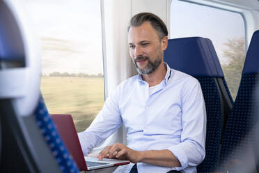 Mature man sitting in a train, using laptop - FKF03556