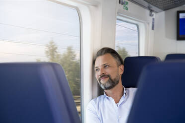 Mature man sitting in a train, looking out of window - FKF03559