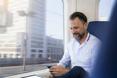 Mature man sitting in a train, using smartphone - FKF03561