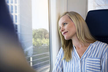 Frau sitzt in einem Zug und schaut aus dem Fenster - FKF03575