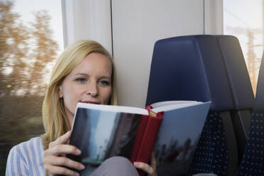 Frau sitzt in einem Zug und liest ein Buch - FKF03576
