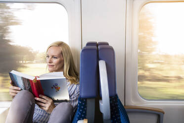 Woman sitting in a train, reading a book - FKF03577