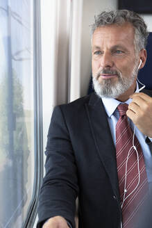 Älterer Geschäftsmann im Zug sitzend, mit Kopfhörern - FKF03581