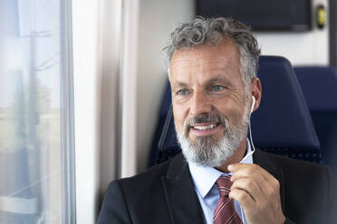 Älterer Geschäftsmann im Zug sitzend, mit Kopfhörern - FKF03582
